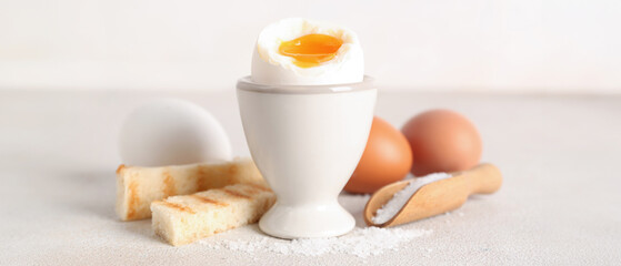 Holder with soft boiled egg, toasted bread and scoop on white table