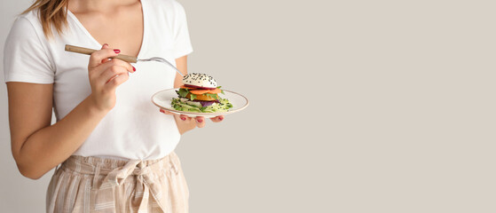 Young woman eating tasty salad on light background