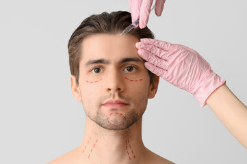 Young man with marked face receiving injection on light background, closeup. Plastic surgery concept