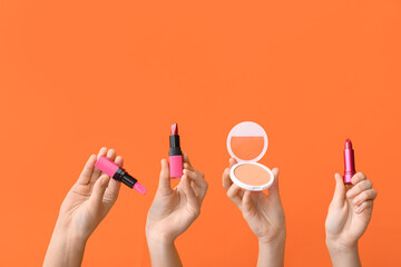 Female hands with lipsticks and powder on orange background