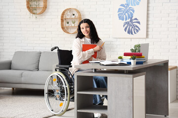 Beautiful female student in wheelchair with laptop and books studying online at home