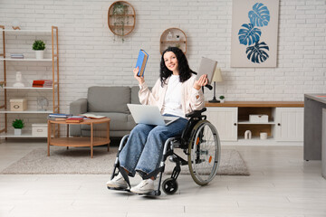 Beautiful female student in wheelchair with modern laptop and books studying online at home