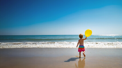 A child playing in the beach with a yellow balloon