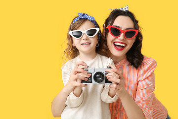 Fototapeta premium Beautiful pin-up woman and her daughter with photo camera on yellow background