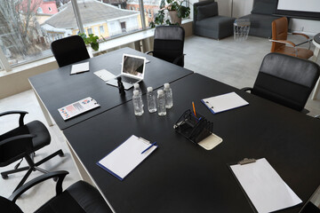 Fototapeta na wymiar Black table, armchairs and stationery prepared for business meeting in modern conference hall