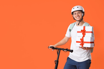 Male courier with gift boxes and kick scooter on orange background