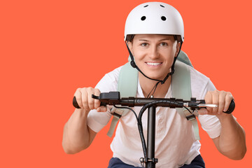 Male courier riding kick scooter on orange background