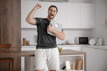 Happy sporty young man with scales in kitchen. Weight loss concept