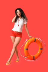 Beautiful young happy African-American female lifeguard with ring buoy on red background