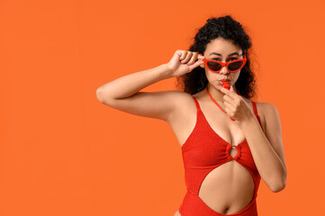 Beautiful young African-American female lifeguard whistling on orange background