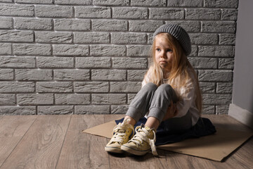 homeless little girl sitting on floor near grey brick wall - obrazy, fototapety, plakaty