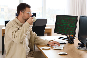 Portrait of male programmer drinking coffee at his workspace in office
