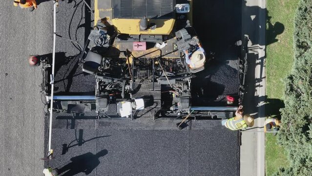 Top-down view of workers and heavy machinery paving a road with fresh asphalt. Workers in high-visibility clothing ensure smooth operations. Footage 4K. 