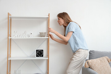 Young woman looking at mold on wall behind shelf unit at home