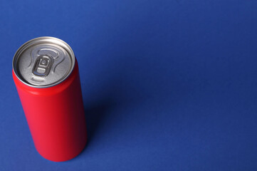 Energy drink in red can on blue background, space for text