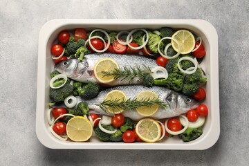 Raw fish with vegetables and lemon in baking dish on grey textured table, top view