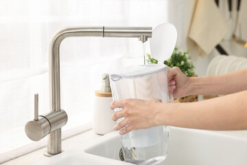 Woman pouring tap water into filter jug in kitchen, closeup