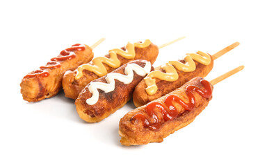 Tasty corn dogs with different sauces on white background