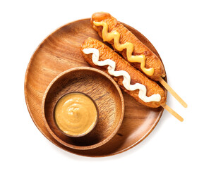 Wooden plate with tasty corn dogs and bowl of mustard on white background