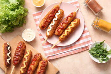 Wooden board and plate of tasty corn dogs with different sauces on beige background