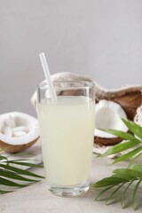 Glass of coconut water, palm leaves and nuts on light table
