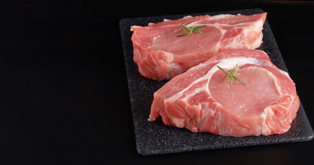 Raw pork steak with rosemary on a black table