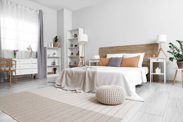 Interior of stylish modern bedroom with big bed, shelving units, chest of drawers and bedside tables