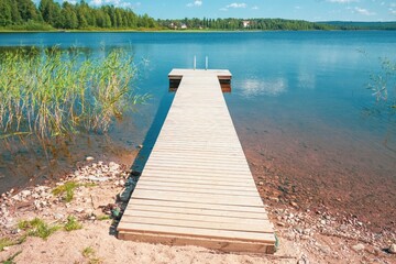 Tranquil scene of a wooden dock stretching out into a peaceful lake surrounded by lush greenery and under the clear blue sky with fluffy white clouds on a sunny summer day
