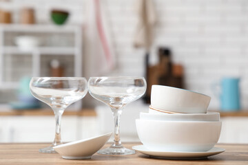Stack of white clean tableware and glasses on wooden table in kitchen