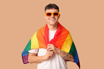 Handsome young happy man with LGBT flag on beige background