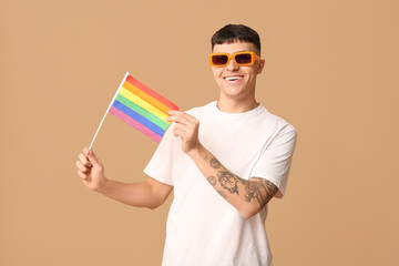 Handsome young happy man with LGBT flag on beige background