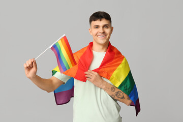 Handsome young happy man with LGBT flags on grey background