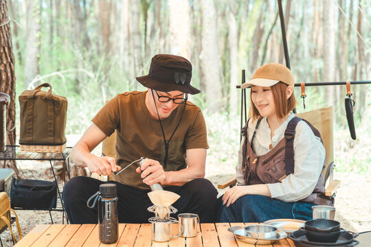 キャンプ場でコーヒーミルを使ってコーヒーを淹れる夫婦キャンパー・カップル・男女
