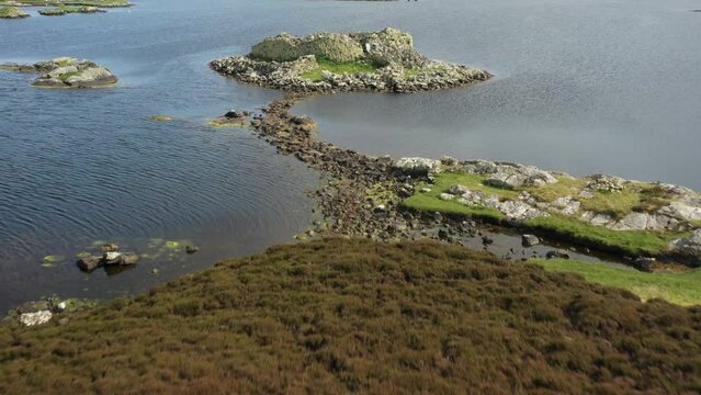 Dun Torcuill prehistoric Iron Age galleried broch aka dun on island in tidal Loch an Duin, North Uist, Hebrides. View South showing causeway to shore. Video aerial drone moving forward