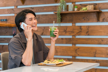 カフェ・学食で食事中にスマホで通話・電話する若いアジア人男性
