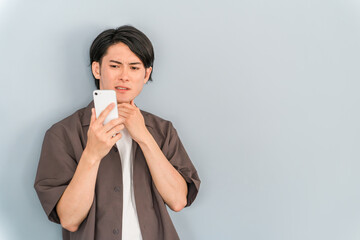 スマホを使う若いアジア人男性（困る・悩む・迷う・考える）
