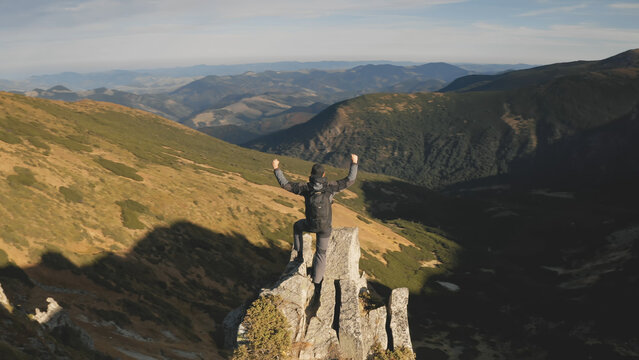 Traveler climb on mountain rock top aerial. Sun nature landscape. Man rising up and waving hands at mount stone peak. Mountaineering travel lifestyle. Cinematic Carpathians ridges, Ukraine, Europe