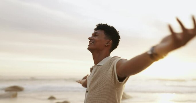 Beach, sunset and man with smile for freedom in vacation, weekend holiday and journey in California. Summer, male person and happy with raised hands in ocean for fresh air, relax or peace outdoors