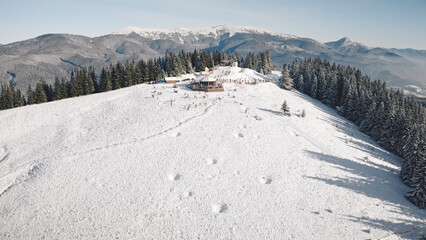 Aerial winter resort at snow mountain forest. Tourists landmark at nature landscape. Frost and cold sunny day. Sun shine above ski slope. People active vacation at Carpathian, Bukovel, Ukraine, Europe