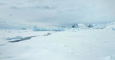 Fly over snow hill in Antarctica winter landscape. Frozen polar ocean with melted cracked river. Glacier and iceberg stuck in ice coast bay. Mountain range in background. Arctic travel and exploration