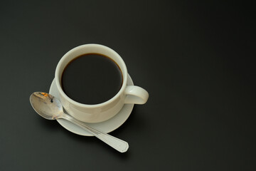 A cup of black coffee with a spoon on a saucer on a black isolated background.