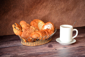 A basket with an assortment of various homemade pastries and a cup of hot tea on a wooden table.