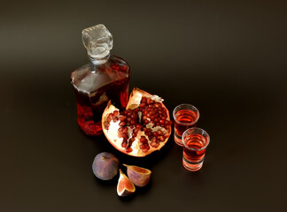 Fig-pomegranate liqueur on a black background, strong alcohol in a bottle and two shots, ripe fruits nearby.