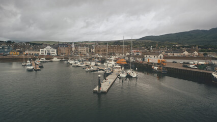 Ships, yachts at sea bay aerial. Cityscape with ancient architecture landmark at ocean pier town Campbeltown, Scotland, Europe. Dramatic streets: old buildings at highway with driving cars at dusk day