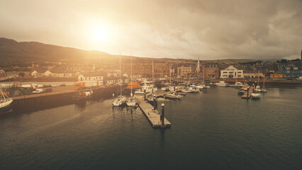 Sun over ships, yachts at sea bay aerial. Port cityscape with ancient architecture landmark at ocean coast of Campbeltown, Scotland, Europe. Urban streets with old buildings at traffic highway