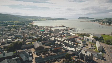 Slow motion cityscape at sea bay aerial. Modern buildings at traffic highway. Downtown streets at green pastures with animals. Ships and yachts at wharf of Campbeltown city, Scotland, Europe