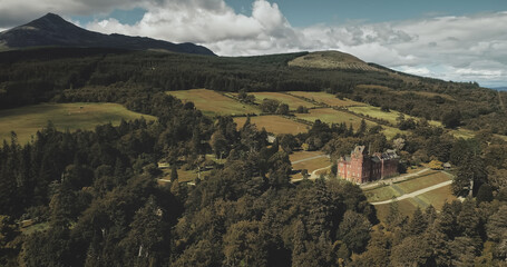 Scotland's mountains, old castle aerial panning shot: designed landscapes of garden and parks near building. Beautiful woods, hills, valleys in horizon at summer day. Dramatic scenery view