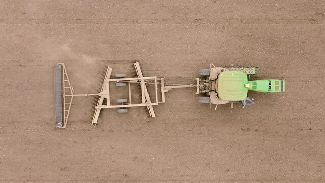 Aerial perspective of a modern tractor with a tiller attachment actively turning over soil, preparing for a new crop season. Footage 4K. 