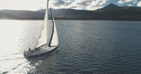 Sail boat yachting at open sea harbor with sun reflection aerial. Closeup of yacht cruise with passengers. Epic sailboat at ocean with travelers tour. Summer vacation on sailboat at Scotland, Europe