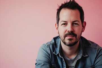 Portrait of a handsome man with a beard and mustache in a denim jacket on a pink background